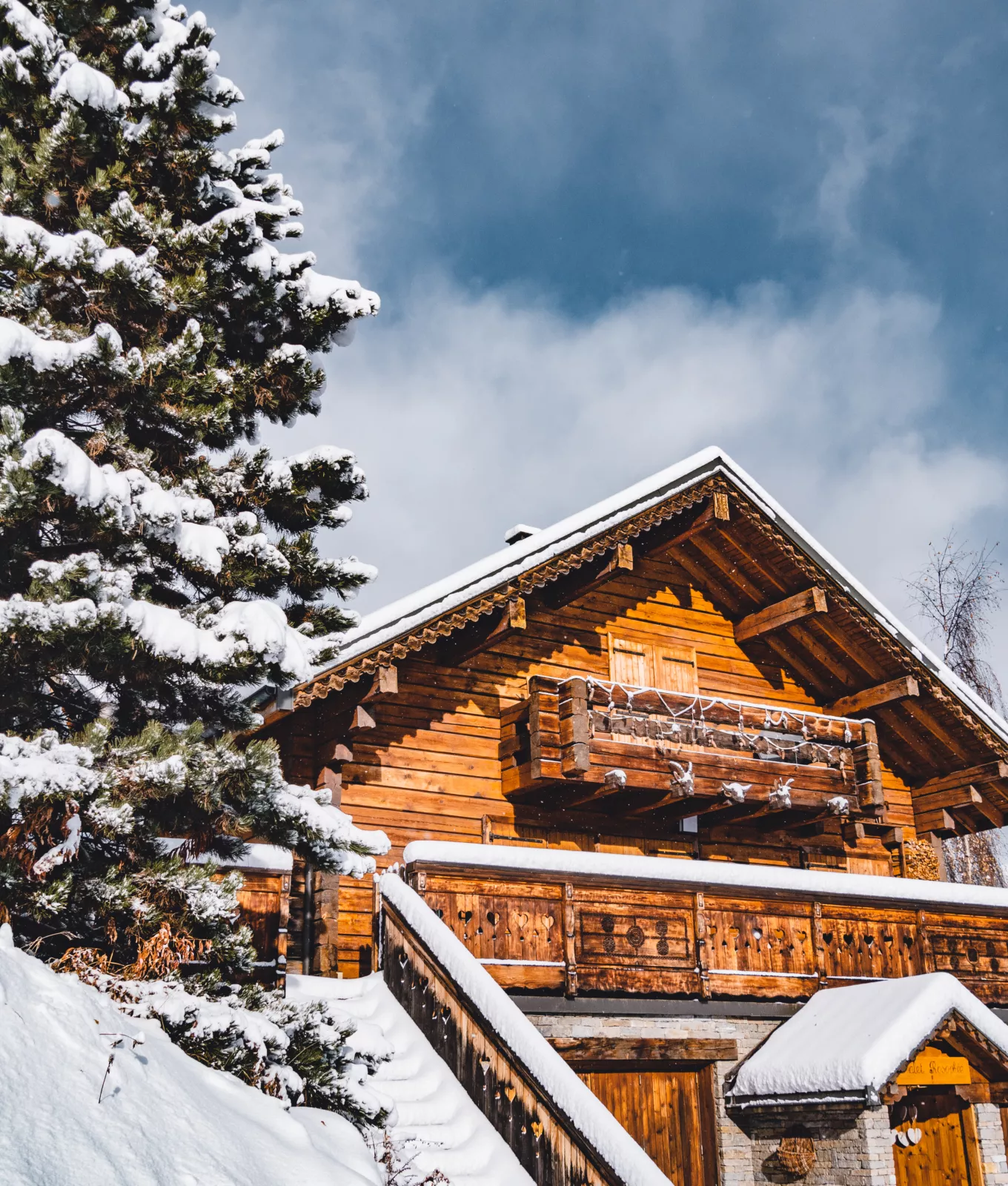 Chalet en bois au Corbier recouvert de neige, avec un ciel nuageux en arrière-plan et des sapins enneigés.